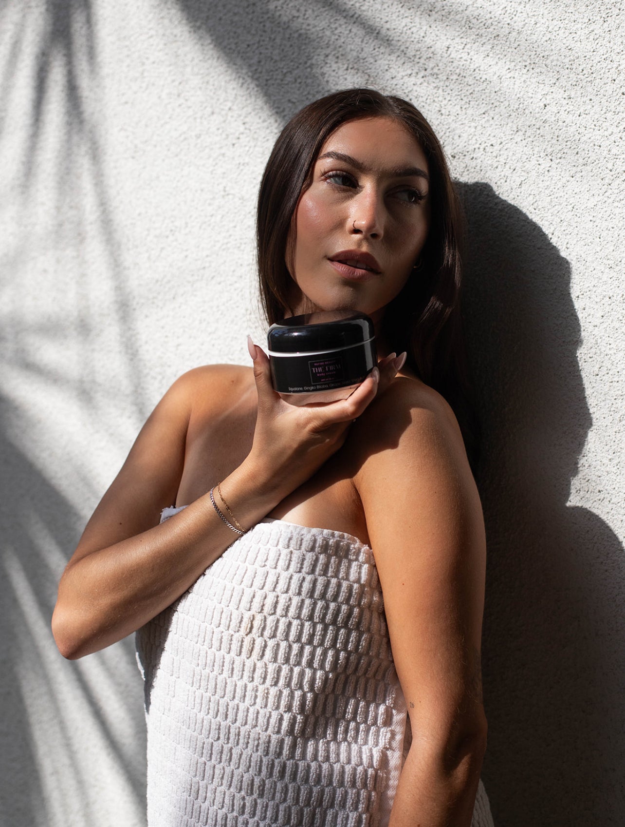 Model holding the FIRM Body cream in front of a white background 